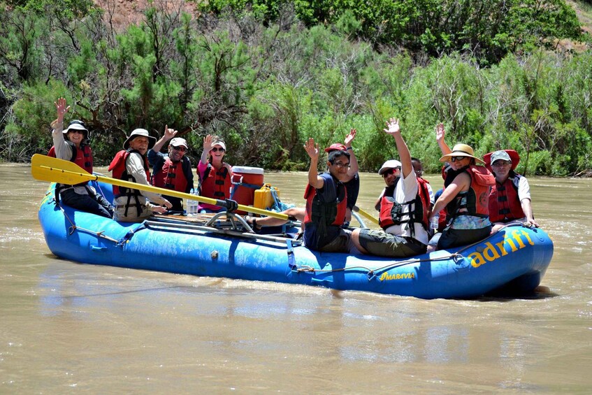 A group of people in a blue inflatable raft on a river, wearing life jackets and paddles. 1