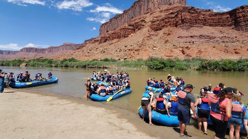 People in blue inflatable rafts on a river, with a rocky canyon in the background. 2