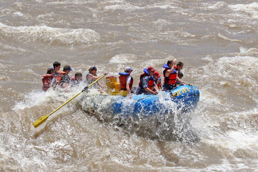 A group of people in a blue raft navigating through rough, muddy waters. 5
