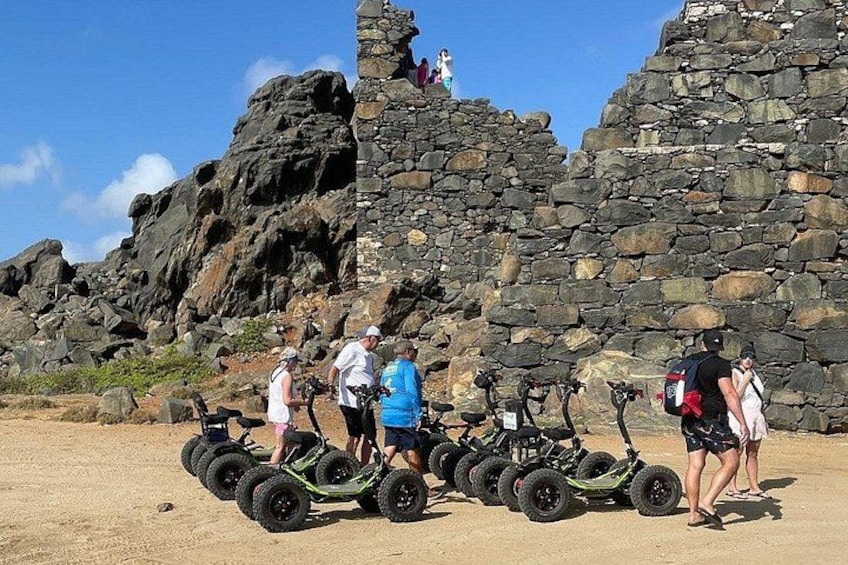 Un grupo de personas en una playa arenosa con ruinas de piedra al fondo. 5