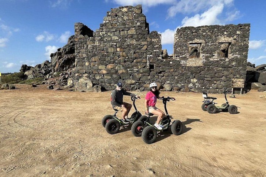 Dos personas montando segways por un sendero de tierra con unas ruinas de piedra al fondo. 3