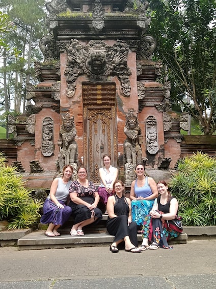 Un groupe de personnes est assis devant un temple orné de sculptures complexes et doté d’une grande porte en bois. 2
