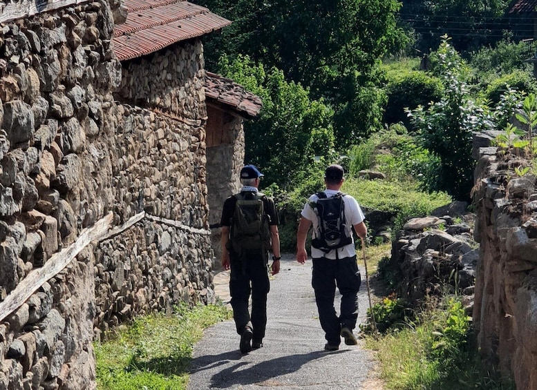 Dos excursionistas caminando por un sendero de piedra al lado de un edificio con tejado de tejas rojas. 1