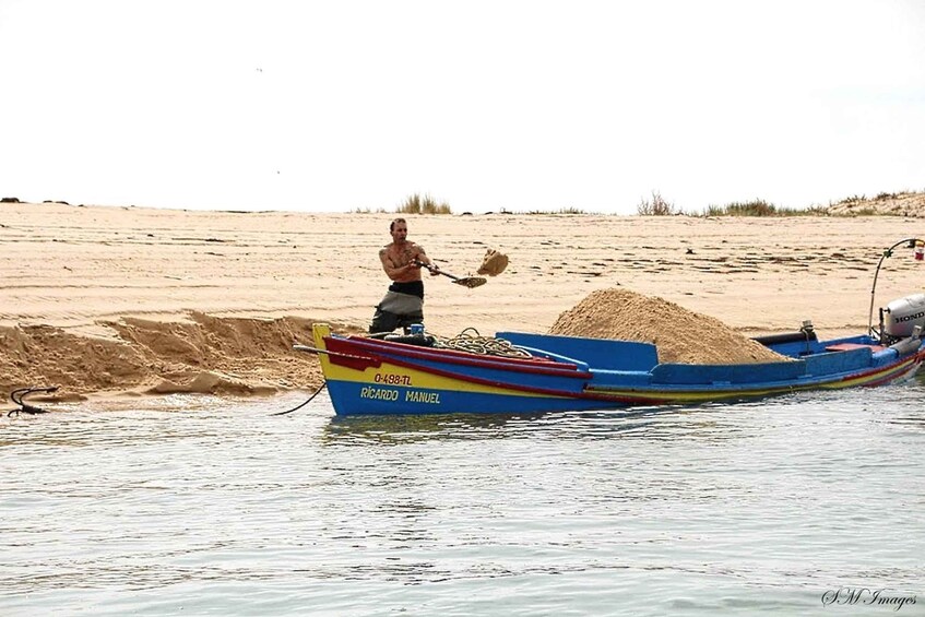 A man in a boat on a sandy shore, holding a net. 3