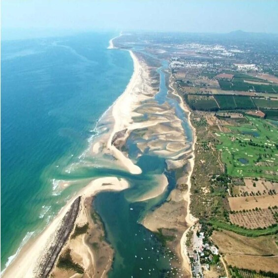 An aerial view of a coastal area with a sandy beach, a river delta, and agricultural fields. 1