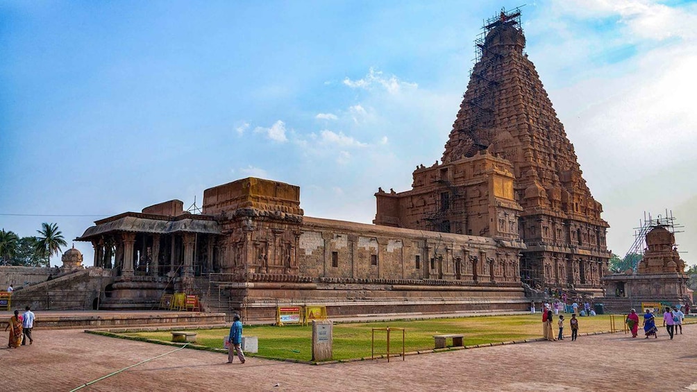 A large temple with a tall spire, surrounded by a paved area with people walking around. 4