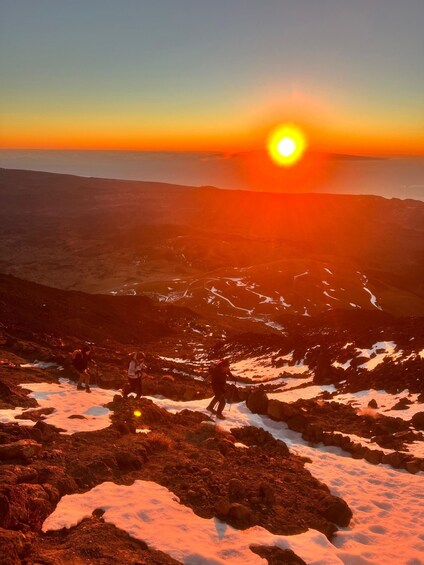 A sunset over a mountainous landscape with hikers on a snow-covered trail. 5
