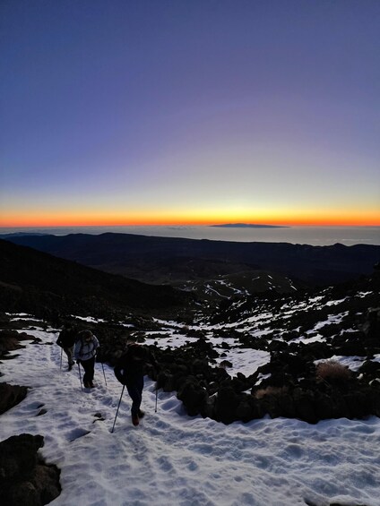 A hiker on a snowy mountain trail with a sunset in the background. 3