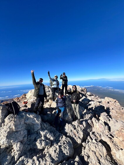 A group of hikers on a rocky mountain peak with a clear blue sky. 4