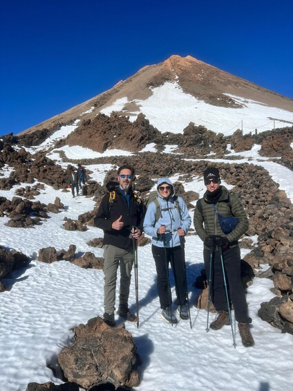 Three people standing on a snowy mountain with rocky terrain and a clear sky. 2