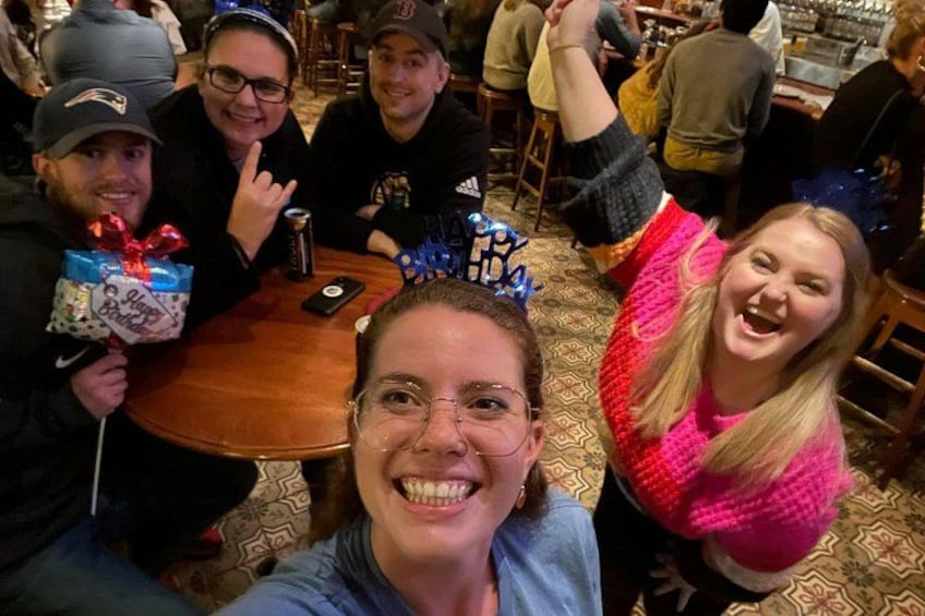 Un grupo de personas en un restaurante con una mesa redonda, algunas sosteniendo regalos, y un ambiente festivo. 4