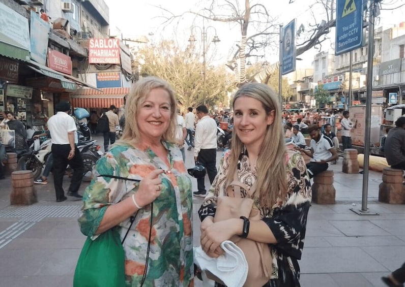 Two women standing on a busy street with shops and pedestrians in the background. 3