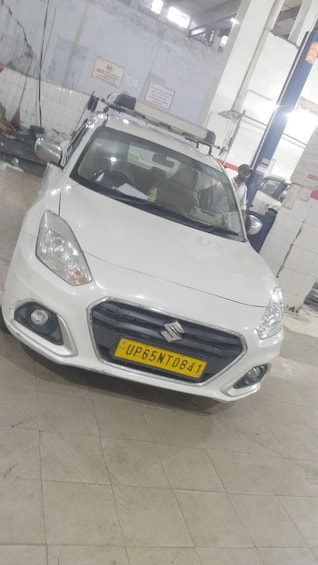 A white Suzuki car with a yellow license plate in a garage. 2