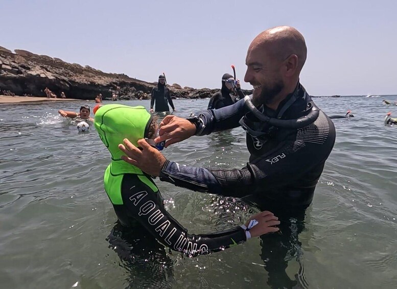 A person in a wetsuit assisting another in a green flotation device in the water. 2