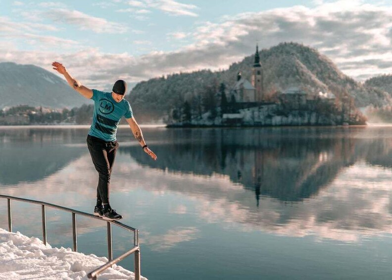 A person balancing on a railing by a calm lake with a church on a hill in the background. 1