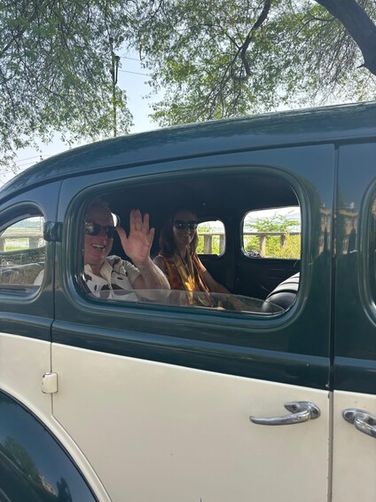 A vintage car with two people waving from the window. 3