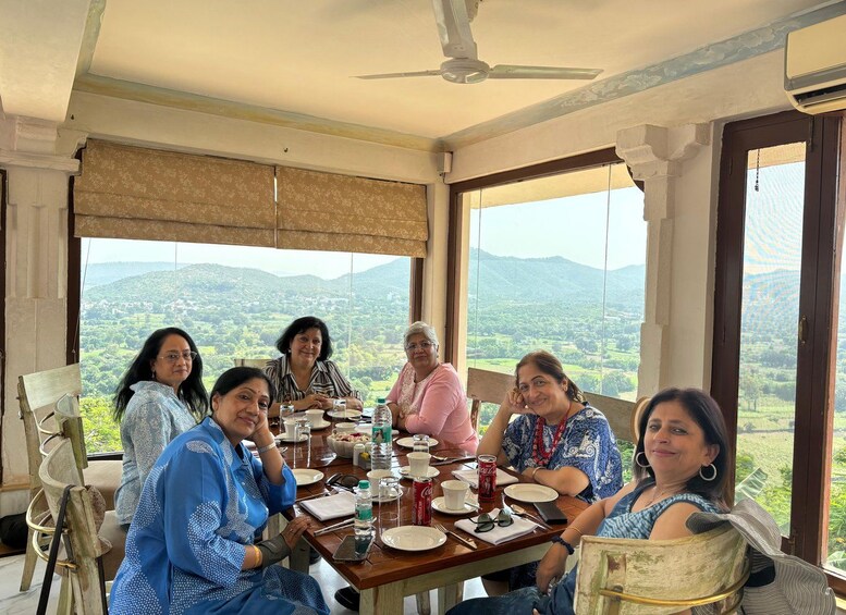 A group of people seated around a table in a room with large windows overlooking a mountainous landscape. 4