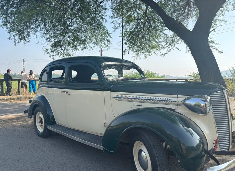 A vintage car parked on a road with trees and a clear sky in the background. 1