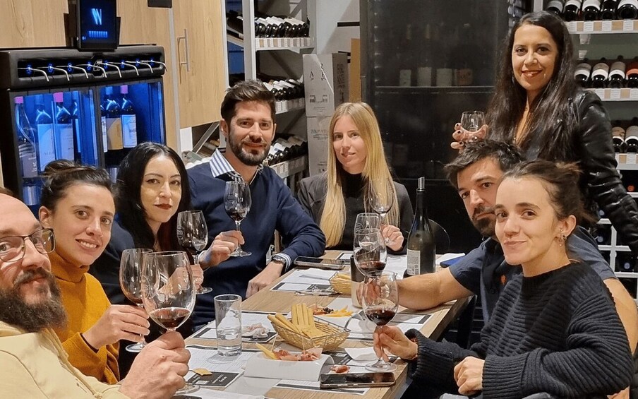 A group of people seated at a table with wine glasses, surrounded by shelves of wine bottles. 2