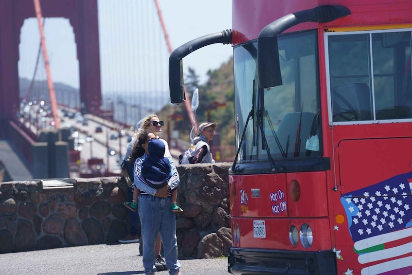 A red bus with an American flag design parked on a street with a stone wall and a bridge in the background. 5