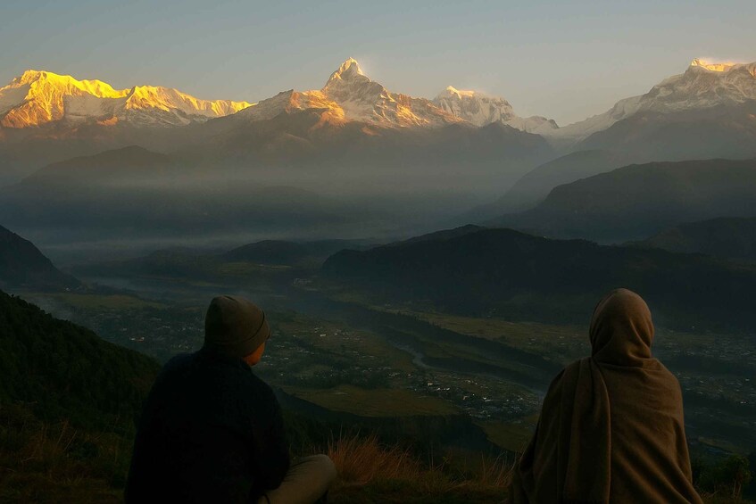 Deux personnes sont assises sur une montagne, d’où elles dominent une vallée, avec des sommets enneigés en arrière-plan. 5