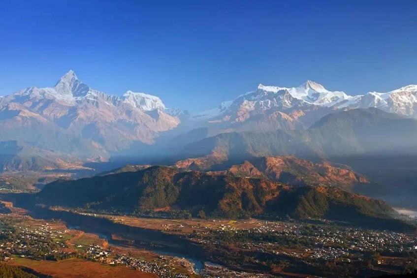 Un paysage montagneux, avec des sommets enneigés et une vallée traversée par une rivière, où se trouve une ville. 4