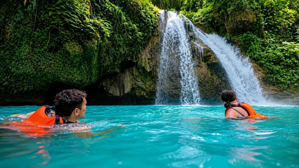 Two people in a clear blue pool with a waterfall in the background. 2