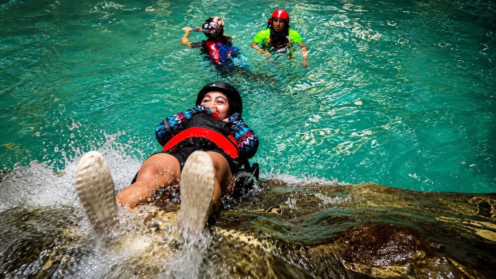 A person in a water slide with clear turquoise water, wearing a helmet and a life jacket. 4