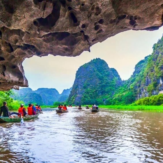 A river with people in boats, a large rock formation, and green hills in the background. 2