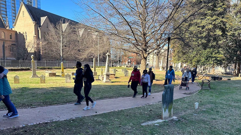Un grupo de personas caminando por un sendero pavimentado en un parque, con árboles y un edificio al fondo. 2