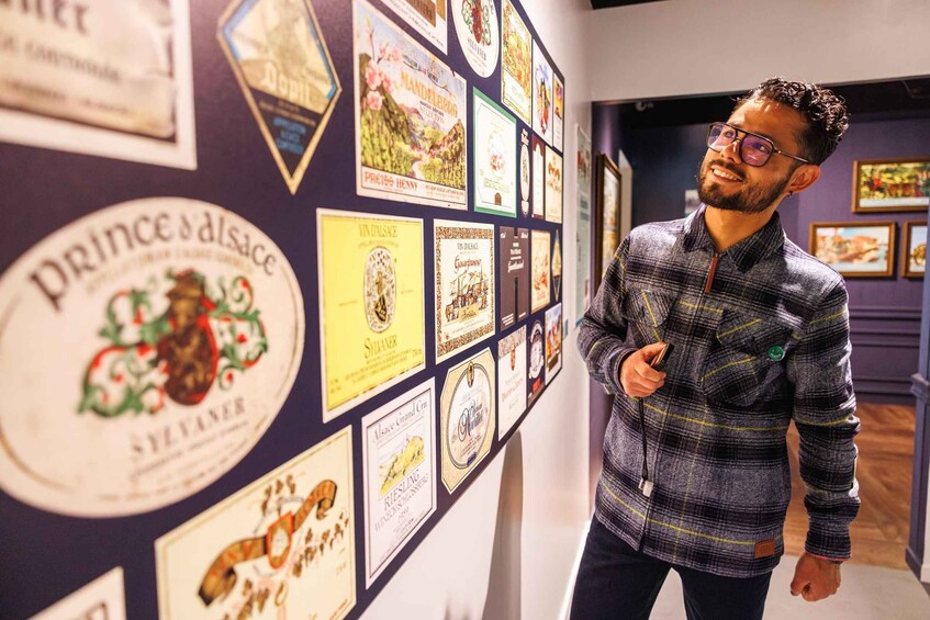 A person standing in a hallway with a wall decorated with various wine labels and posters. 2