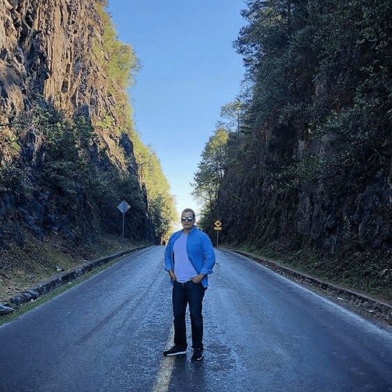 A person standing on a road flanked by steep cliffs and dense foliage. 3