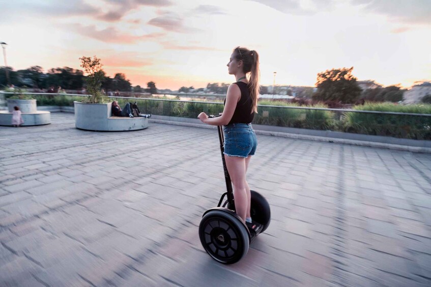 A person riding a hoverboard on a paved area with a sunset in the background. 2