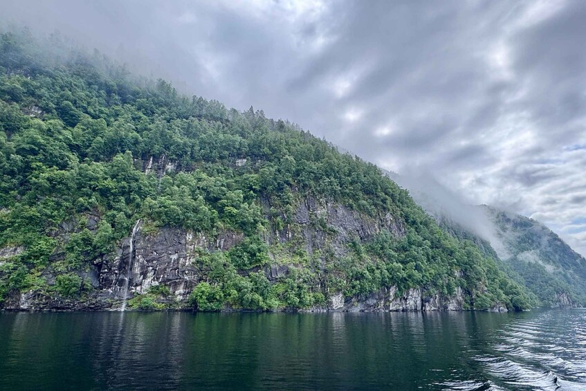 A mountainous landscape with dense green forests and a calm body of water reflecting the sky. 5