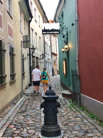 A cobblestone street with buildings, a black statue, and two people walking. 3