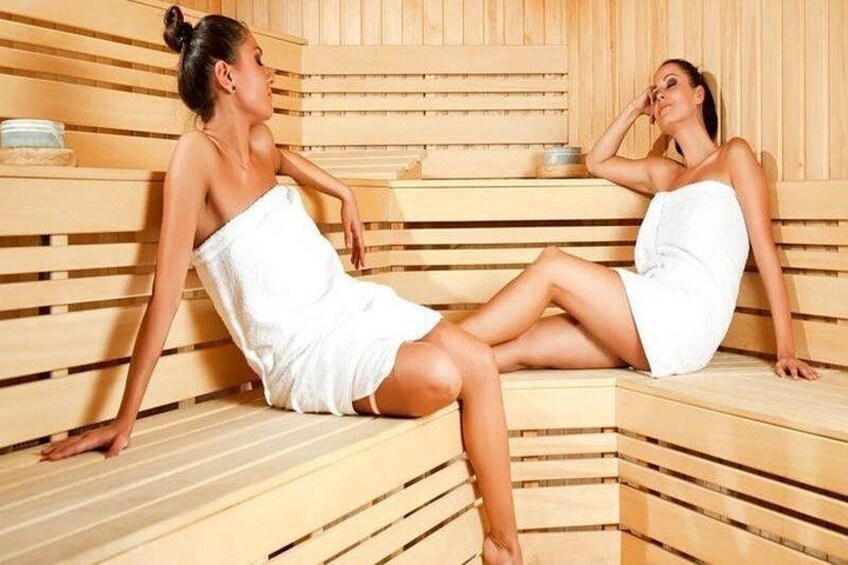 Two individuals in a sauna with wooden benches and benches. 4