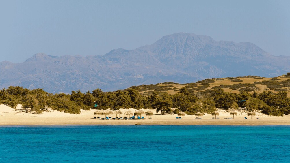 A beach with clear blue water, a sandy shore, and a backdrop of mountains. 5