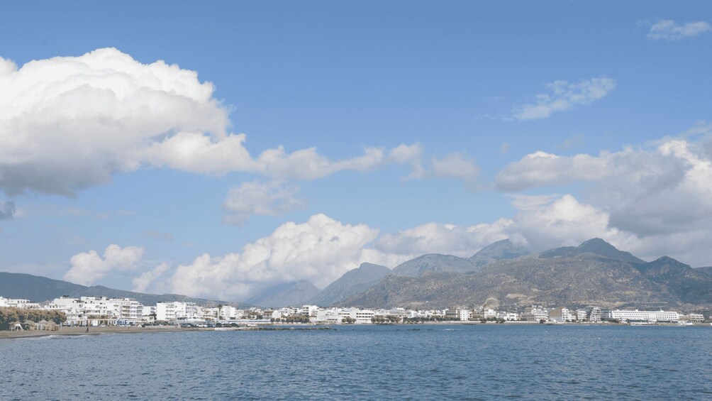 A coastal city with white buildings, a calm sea, and mountains in the background. 4