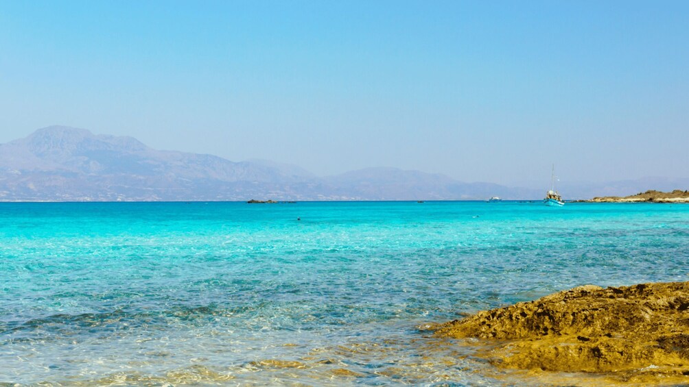 A clear turquoise sea with rocky shorelines and distant mountains. 2
