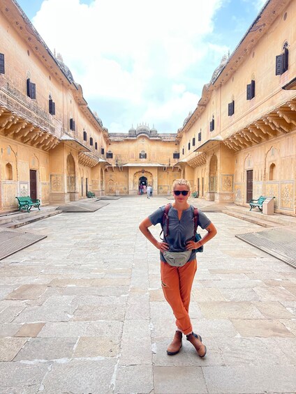 A person standing in a courtyard with ornate buildings and stone flooring. 5