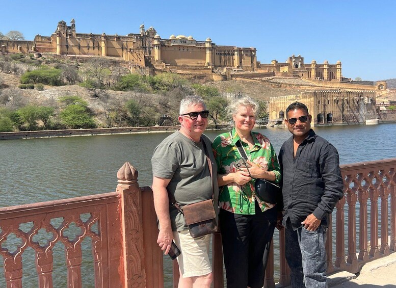 Three people standing on a bridge with a historic fort in the background. 2