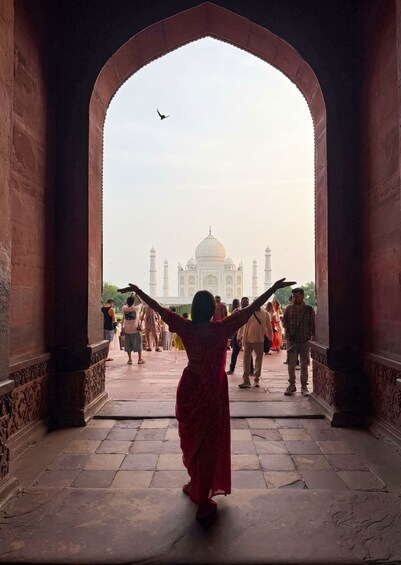 A person in a red dress with arms outstretched, facing the Taj Mahal. 5