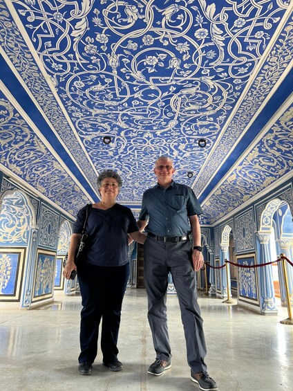 Two people standing in a room with ornate blue and white ceiling decorations. 2