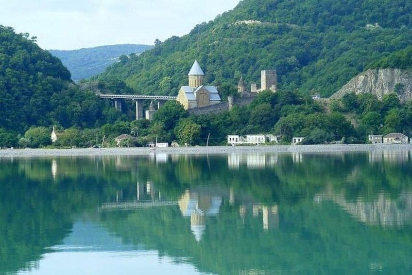 A serene lake with a historic building featuring a dome and bell tower, surrounded by lush greenery and hills. 4