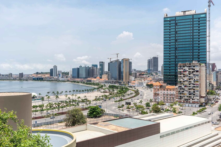 A coastal cityscape with a prominent blue high-rise building, palm-lined promenade, and a calm sea. 4