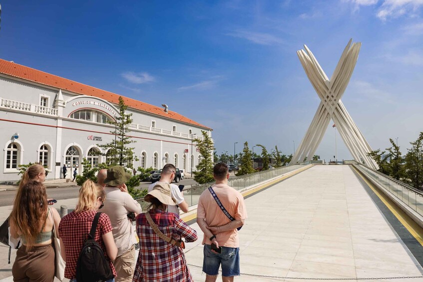 A group of people standing on a bridge with a modern sculpture in the background. 1