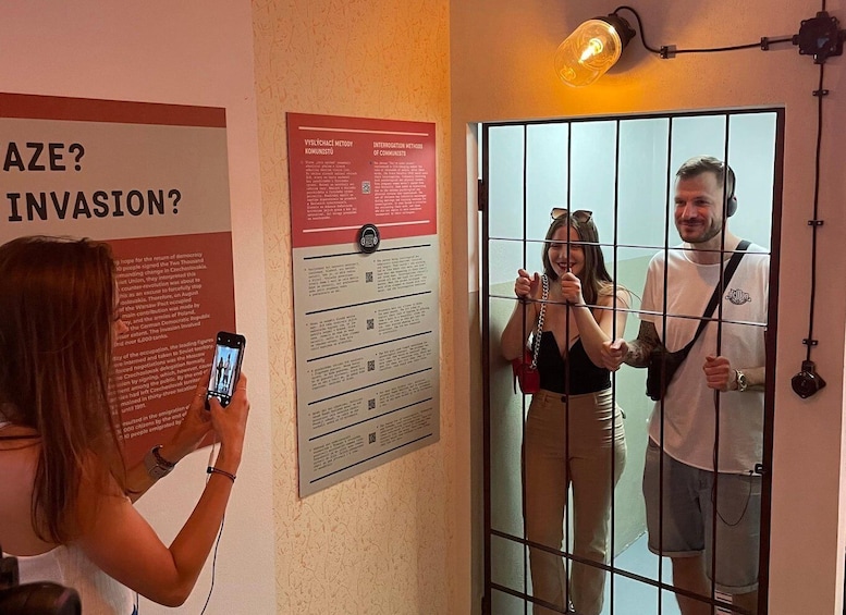 A person taking a photo of a poster and a man standing behind a barred door. 5