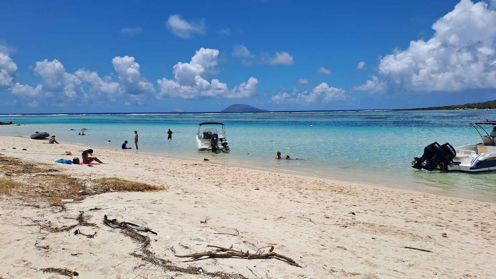 A beach with people sunbathing, swimming, and a boat parked on the shore. 2
