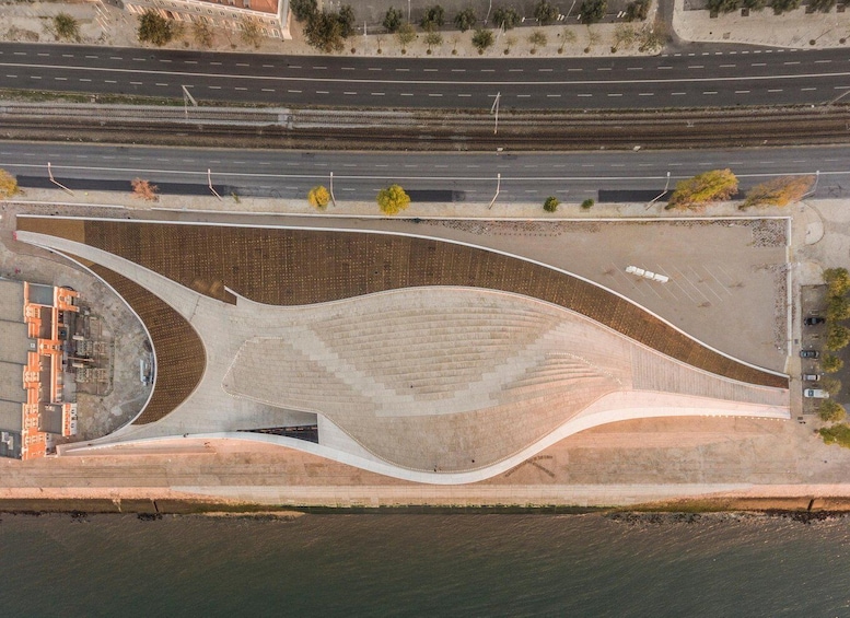 An aerial view of a modern architectural structure with a curved design, adjacent to a road and railway tracks. 4