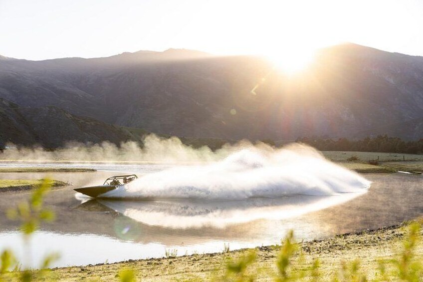 A jet ski creating a large spray of water on a lake with mountains in the background. 1